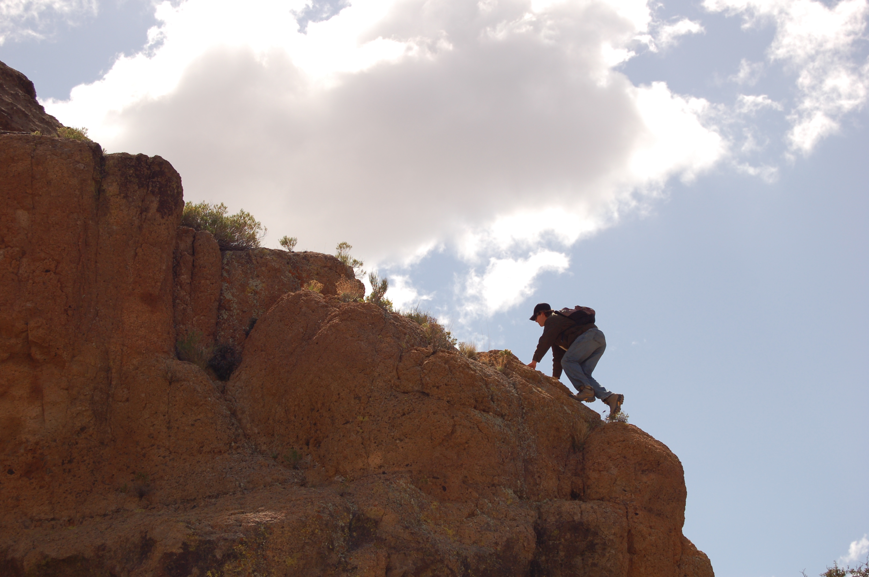 A man climbs on a cliff edge looking for rock samples